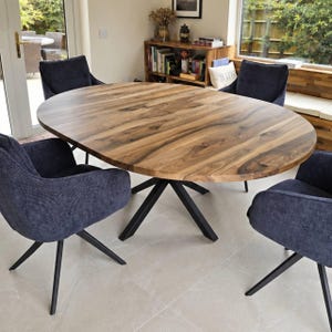 May include: An oval dining table with a natural wood grain top and a black metal star-shaped base, surrounded by four dark blue upholstered chairs with black metal legs. The table features a visible seam indicating an extendable design.