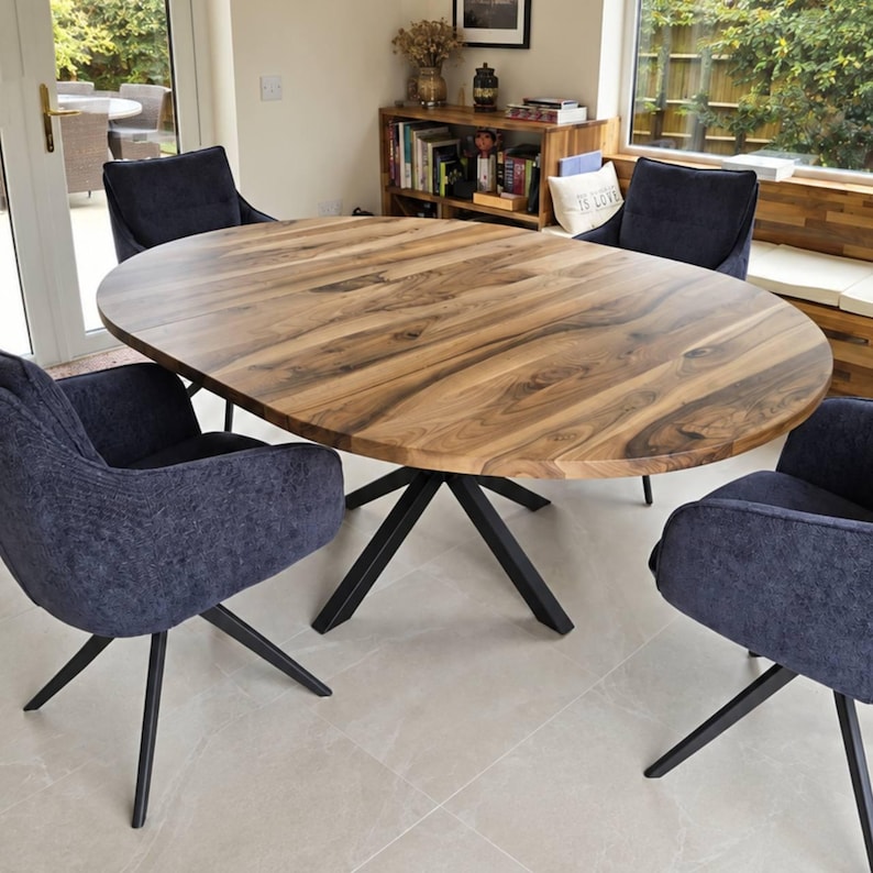 May include: An oval dining table with a natural wood grain top and a black metal star-shaped base, surrounded by four dark blue upholstered chairs with black metal legs. The table features a visible seam indicating an extendable design.