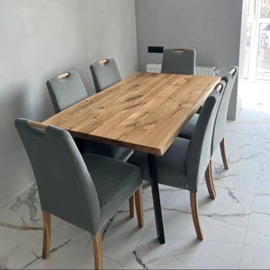 May include: A rectangular dining table with a natural light brown wood grain top and black metal legs, surrounded by six upholstered chairs. Each chair features a light gray fabric seat and backrest with a light wood handle on the top edge.