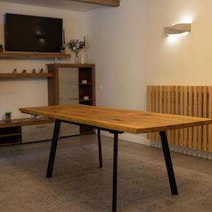 May include: A rectangular dining table featuring a thick, natural-toned wooden top with visible grain patterns and knots. The table is supported by four angled, matte black metal legs that provide a sturdy base for the heavy wooden surface.