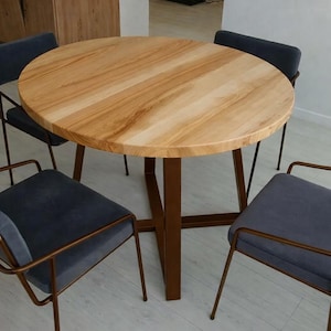 May include: A round wooden dining table with a light brown finish, supported by a dark brown metal base. Four chairs with dark gray seats and bronze-colored metal frames surround the table. The table's diameter is approximately 48 inches.