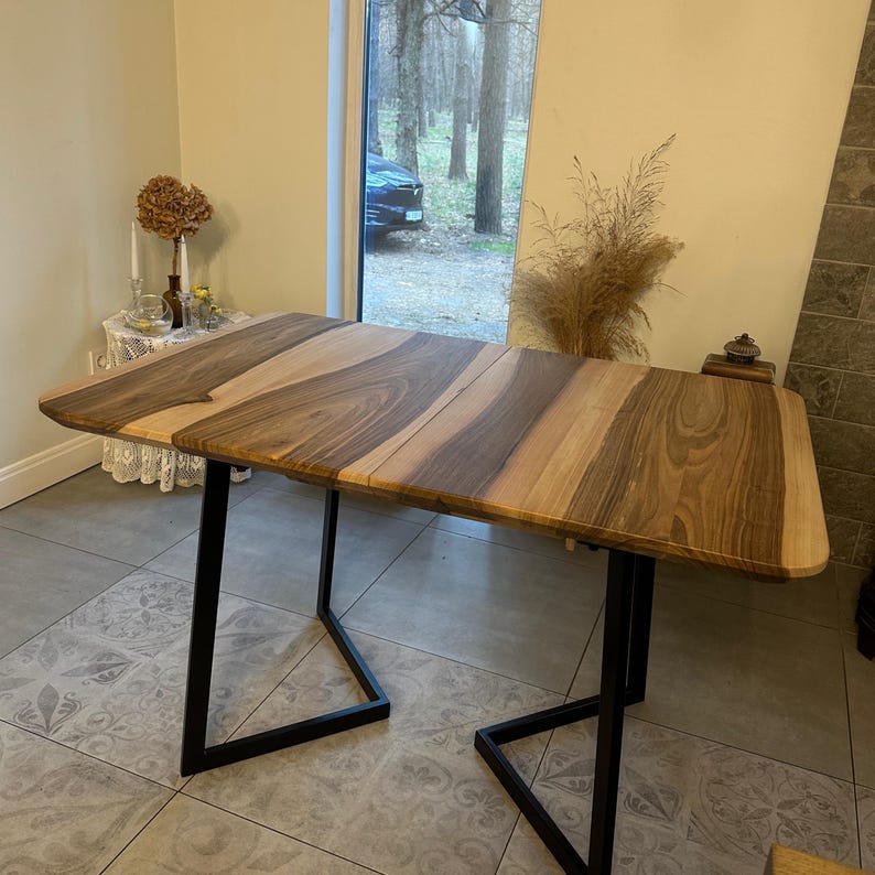 K&ouml;nnte beinhalten: Ein rechteckiger Holztisch mit einem gestreiften Muster in Braun- und Beiget&ouml;nen. Der Tisch hat schwarze Metallbeine. Der Tisch ist etwa 152 cm lang und 76 cm breit.