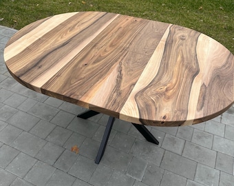 May include: An oval dining table featuring a natural wood grain surface with contrasting light and dark brown tones. The tabletop is constructed from multiple joined planks and is supported by a black metal base with four angled legs.