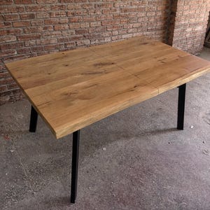 Puede incluir: Una mesa rectangular de madera con acabado marrón claro. La superficie de la mesa está dividida en cuatro secciones y descansa sobre cuatro patas de metal negro. La mesa está contra una pared de ladrillo.