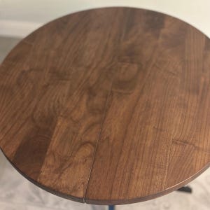 Peut inclure: Une table ronde en bois avec une finition marron fonc&eacute;. Le plateau de table pr&eacute;sente un motif de grain de bois visible. Il s'agit probablement d'une petite table d'appoint, d'environ 76 cm de diam&egrave;tre.