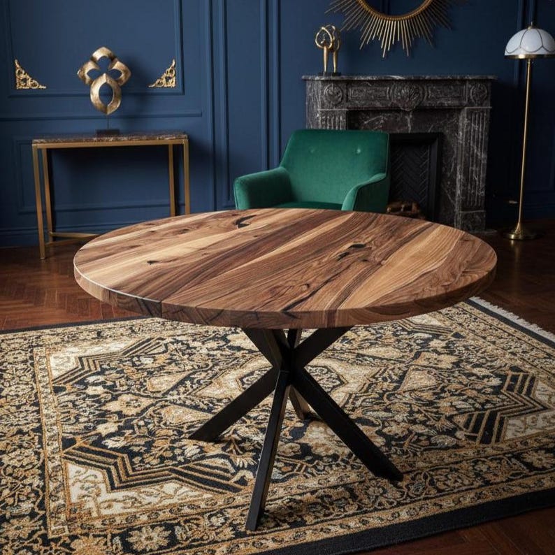 May include: A round dining table featuring a natural wood grain top with visible dark knots and swirling patterns, supported by a black metal base with four intersecting legs that form an X-shape at the center point beneath the tabletop surface.