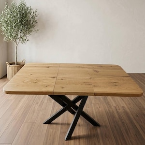 Pode incluir: Uma mesa de jantar retangular com um tampo de madeira castanho-claro com veios visíveis e uma base de metal preto com pernas cruzadas. A superfície da mesa apresenta nós de madeira visíveis e uma costura central, indicando um design extensível.