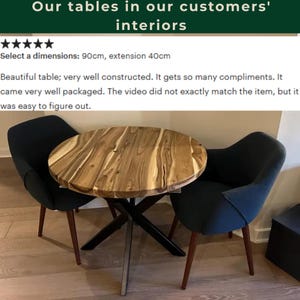 May include: A round wooden dining table with a natural grain pattern and a black metal X-shaped base, accompanied by two dark charcoal upholstered chairs with tapered wooden legs. The text reads: Our tables in our customers' interiors.