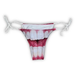 Może przedstawiać: Nowatorski dół od bikini z dużym, szczegółowym nadrukiem szeroko otwartych ust z jasnymi białymi zębami i czerwonym wnętrzem. Bikini ma białe sznurki po każdej stronie.
