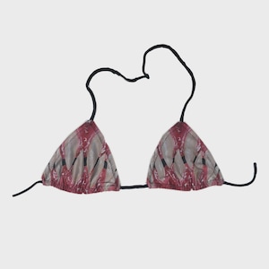 Puede incluir: Top de bikini triangular con un estampado de líneas rojas y negras sobre un fondo beige. El top tiene tirantes negros que se atan al cuello y a la espalda. El traje de baño está diseñado para un ajuste cómodo.