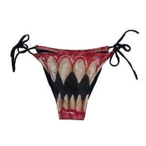 May include: Black and red underwear featuring a graphic of a wide-open mouth with large, off-white teeth. The underwear has black tie strings on each side.