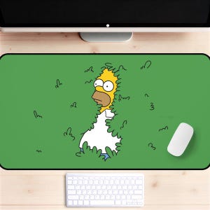May include: Green rectangular mousepad featuring Homer Simpson peeking from behind a bush. The cartoon character has yellow skin, a white shirt, and blue pants. A white computer mouse and keyboard are also visible.