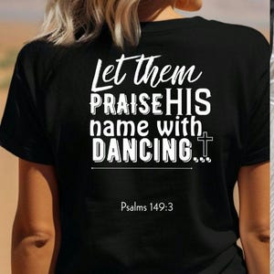 May include: Black t-shirt with white text that reads "Let them praise His name with dancing..." and "Psalms 149:3" below. The shirt is worn by a person with blonde hair.
