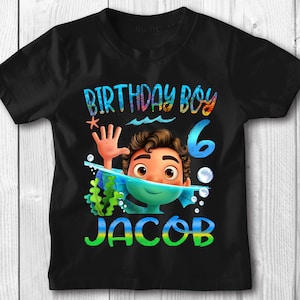 May include: Black t-shirt with a colorful graphic of a boy with a snorkel and flippers in the water. The text "Birthday Boy 6 JACOB" is on the shirt.