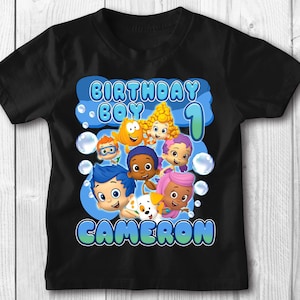 May include: Black t-shirt with a blue, yellow, and white graphic of the characters from the cartoon "Bubble Guppies". The graphic includes the text "Birthday Boy 1" and the name "Cameron".