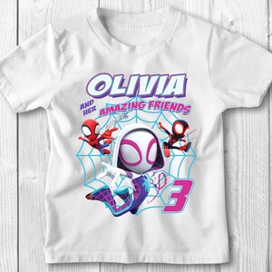 May include: White t-shirt featuring a graphic of Spider-Gwen and two other Spider-Man characters. The text "Olivia and her amazing friends" is printed on the shirt. The number "3" is also printed on the shirt.