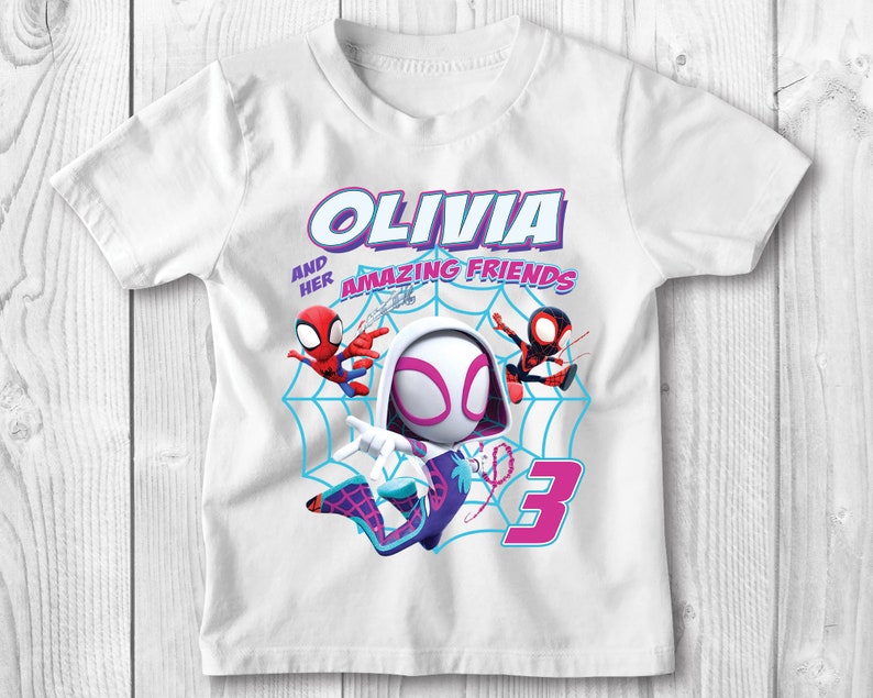 May include: White t-shirt featuring a graphic of Spider-Gwen and two other Spider-Man characters. The text "Olivia and her amazing friends" is printed on the shirt. The number "3" is also printed on the shirt.