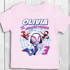 May include: Pink t-shirt featuring a graphic of Spider-Gwen and two other Spider-Man characters. The text "Olivia and her amazing friends" is above the graphic and the number "3" is below the graphic.