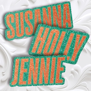 Könnte beinhalten: Drei glitzernde Namensausstanzungen: "SUSANNA", "HOLLY" und "JENNIE". Jeder Name ist in orangefarbenem Glitzer mit einer grünen Glitzerkontur gehalten. Die Namen sind in verschiedenen Winkeln auf einem weißen, strukturierten Hintergrund angeordnet.