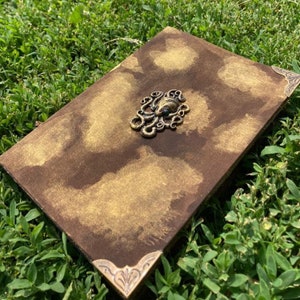 May include: A brown leather-bound journal with gold accents and a decorative metal octopus on the front cover.