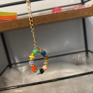 May include: A gold chain with a colorful beaded ring. The beads are in various colors, including red, blue, green, yellow, and black.