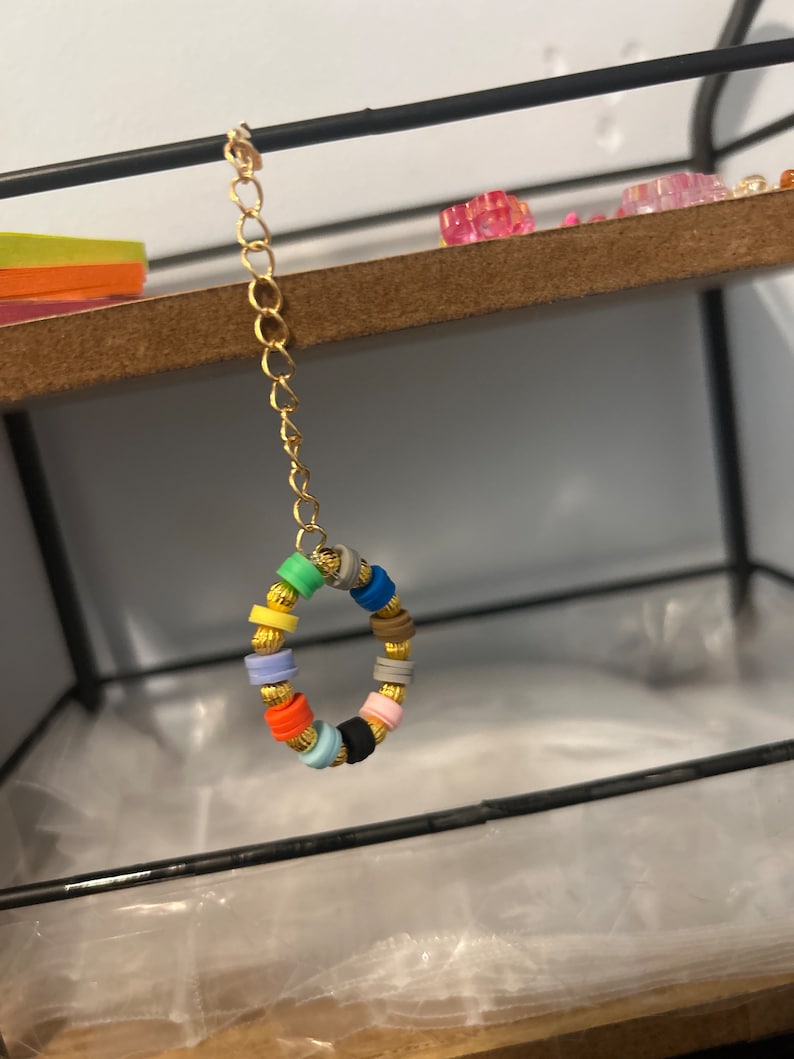 May include: A gold chain with a colorful beaded ring. The beads are in various colors, including red, blue, green, yellow, and black.