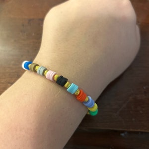 May include: A colorful beaded bracelet with gold spacers. The bracelet is made of small, round beads in various colors, including blue, green, yellow, orange, red, pink, and black. The beads are separated by gold spacers.