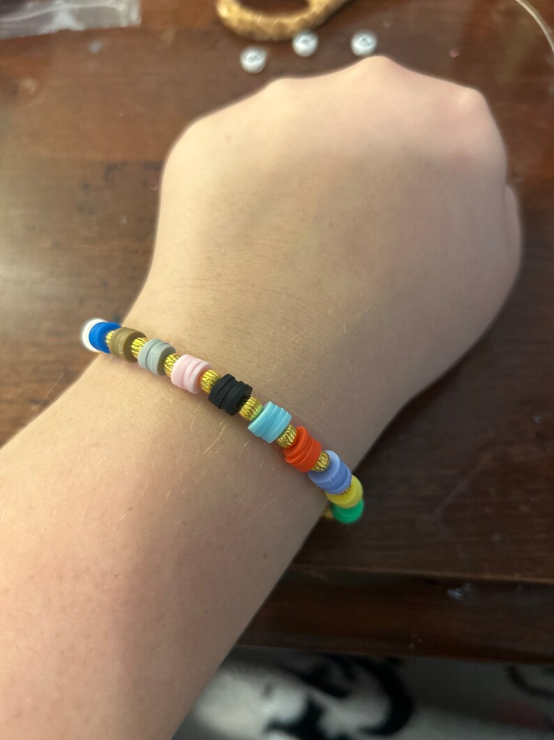 May include: A colorful beaded bracelet with gold spacers. The bracelet is made of small, round beads in various colors, including blue, green, yellow, orange, red, pink, and black. The beads are separated by gold spacers.