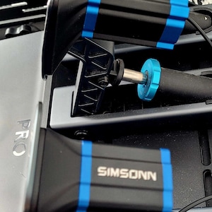 Puede incluir: Un conjunto de pedales de carreras SIMSONN en negro y azul con una etiqueta metálica PRO en el lateral. Los pedales incluyen componentes mecánicos, muelles y anillos de ajuste azules, montados sobre un marco oscuro con cableado visible.