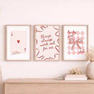 Op de afbeelding: Drie ingelijste kunstdrukken met licht houten frames. De prints tonen een speelkaart, de tekst 'things always work out for me' en een strik met de woorden 'lucky girl club'. Het kleurenpalet omvat roze, rood en wit.