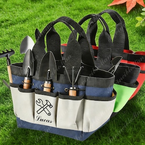 May include: A selection of garden tool bags in blue, white, and red, with black handles. Each bag features multiple pockets and holds various gardening tools, including trowels and a rake. The front bag has a graphic of a wrench and hammer with the name "Lucas".