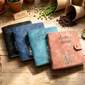 May include: Four leather seed books in black, blue, teal, and coral. Each book has a name and the words "SEED BOOK" printed on the cover, with floral illustrations. The books are arranged on a wooden surface.
