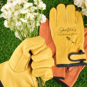 May include: Yellow leather gardening gloves with black trim and the text "Sebastian's Gardening gloves" and a small shovel graphic. The gloves are holding a bouquet of white flowers. Another pair of orange gloves is in the background.