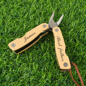 May include: A personalised multi-tool with wooden handles, engraved with "James" and "Best father." The tool features pliers and a leather strap, set against a green background.