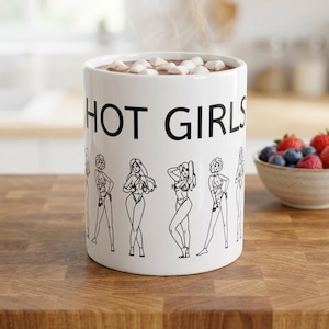 Può includere: Una tazza in ceramica bianca riempita con una bevanda calda e marshmallow. L'esterno presenta il testo nero "HOT GIRLS" stampato sopra una serie di illustrazioni a tratto nero che raffigurano varie figure in costume da bagno.