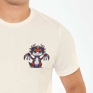 May include: A white t-shirt with a small, cartoon dragon printed on the front. The dragon is red, orange, and purple with blue eyes.