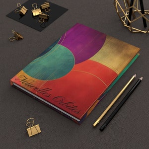 May include: A colorful notebook with a geometric pattern of overlapping circles in shades of red, green, purple, and gold. The notebook cover has the text "Nouvelles Orbites" printed on it.