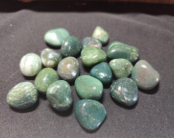 May include: A collection of green moss agate tumbled stones. The stones are smooth and polished, with a variety of green shades and patterns.