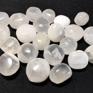 Peut inclure: Une collection de pierres de sélénite blanche roulées. Les pierres sont lisses et polies, avec une apparence translucide.