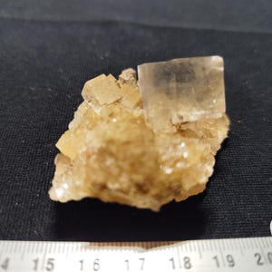 Peut inclure: Spécimen minéral naturel présentant des cristaux de fluorite brun clair. Les cristaux ont une forme cubique et sont disposés sur une matrice de cristaux plus petits et granulaires. Le spécimen est présenté sur un fond sombre.