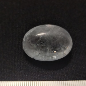 Peut inclure: Un cristal clair de forme ovale avec une apparence légèrement nuageuse. Le cristal a une surface lisse et polie et mesure environ 2,5 cm de diamètre.