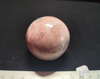 May include: A polished, spherical gemstone, primarily pink with darker gray and black inclusions. The stone is smooth and reflective, suggesting a high-quality finish. The sphere is a decorative item, possibly for display or collection.
