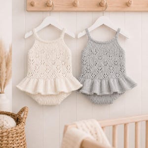 May include: Two sleeveless knit rompers with a delicate leaf-patterned lace design, featuring a ruffled waist and thin straps. One romper is cream-colored, and the other is light gray. Both garments are displayed on white hangers.
