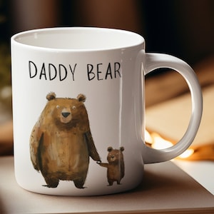 Può includere: Una tazza in ceramica bianca con un orso marrone e un orso marrone più piccolo che si tengono per mano. Il testo "DADDY BEAR" è stampato sulla tazza.