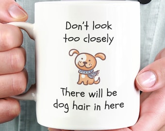 May include: White ceramic mug with a black and white cartoon dog wearing a blue scarf. The mug has the text "Don't look too closely There will be dog hair in here" printed on it.