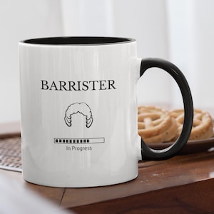 Könnte beinhalten: Weißer Keramikbecher mit schwarzem Innenraum und Griff. Der Becher trägt das Wort "BARRISTER" über einer Grafik einer Perücke und einer Fortschrittsanzeige mit der Aufschrift "In Progress".