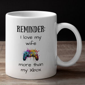 May include: White coffee mug with a black and white graphic that says "REMINDER: I love my wife more than my Xbox". The graphic also includes a colorful video game controller.