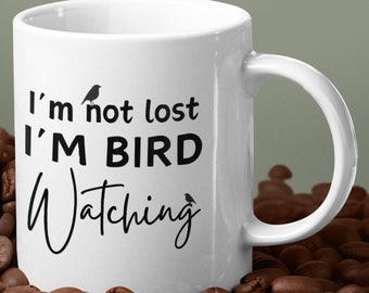 May include: White ceramic coffee mug with black text that reads "I'm not lost I'm bird watching". There are two small bird silhouettes on the mug.