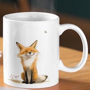 Könnte beinhalten: Weiße Keramiktasse mit einer Cartoon-Illustration eines lächelnden orangefarbenen Fuchses, der sitzt. Eine kleine Biene fliegt über dem Fuchs.