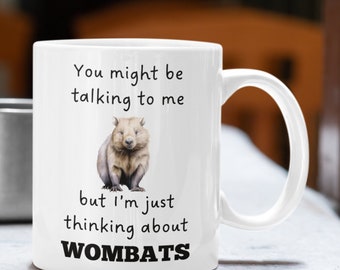 Op de afbeelding: Een witte keramische mok met een zwart-witte illustratie van een wombat. Op de mok staat "You might be talking to me but I'm just thinking about WOMBATS".
